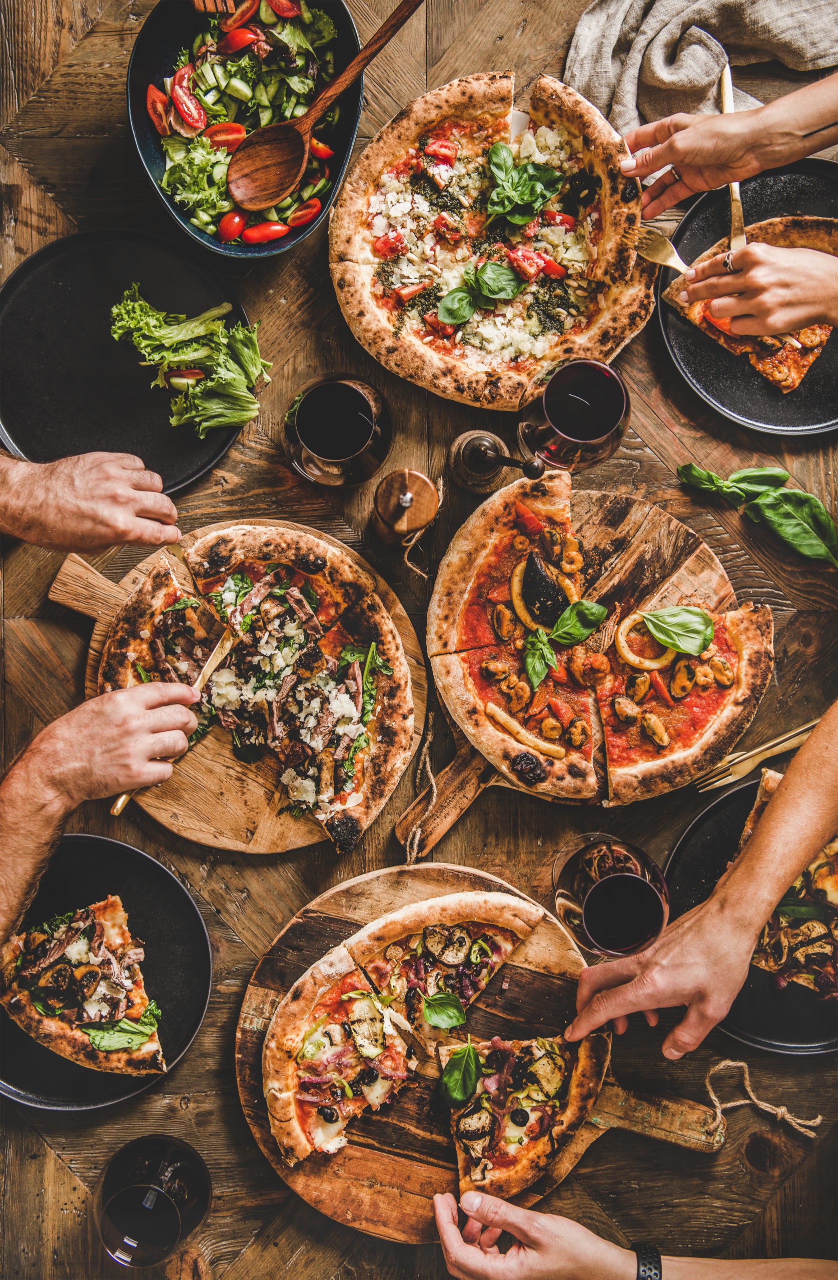 Family or friends having pizza party dinner. Flat-lay of people eating various kinds of Italian pizza and drinking wine over rustic wooden table, top view. Fast-food lunch, gathering or celebration